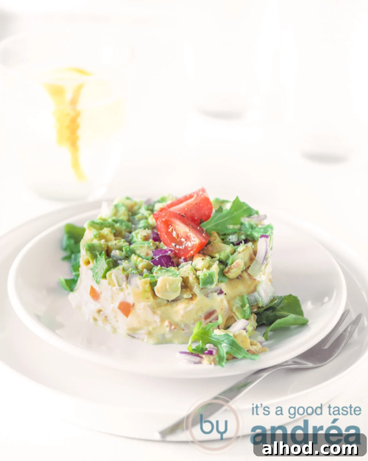 Beautifully presented smoked chicken and avocado salad tower garnished with cherry tomatoes on elegant white plates, perfect for a starter.