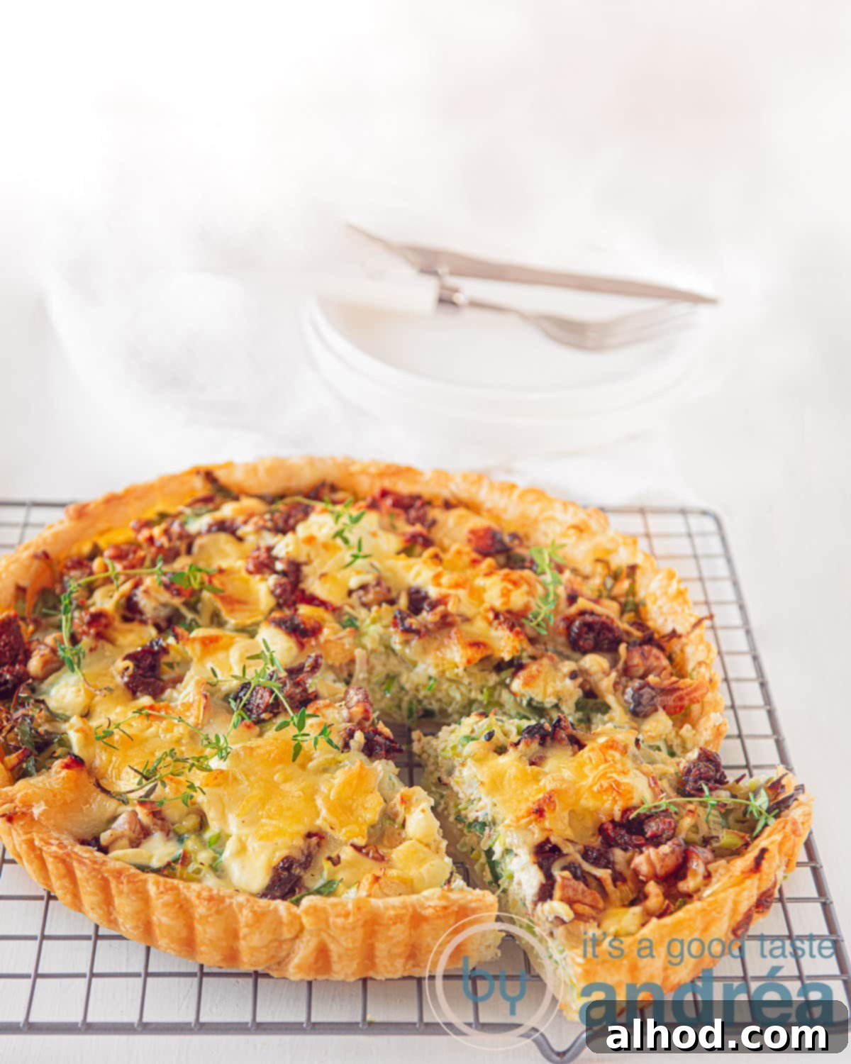 Gourmet Leek Goat Cheese Walnut Quiche 5 A quiche on a wire rack, filled with leeks, goatchees, walnuts and honey. A slice cut of on a white background.