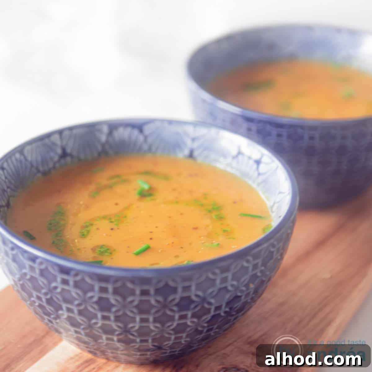 Naturally Creamy Pumpkin Soup 4 A square photo with two blue bowls filled with pumpkin soup with a delicious herbal dressing.