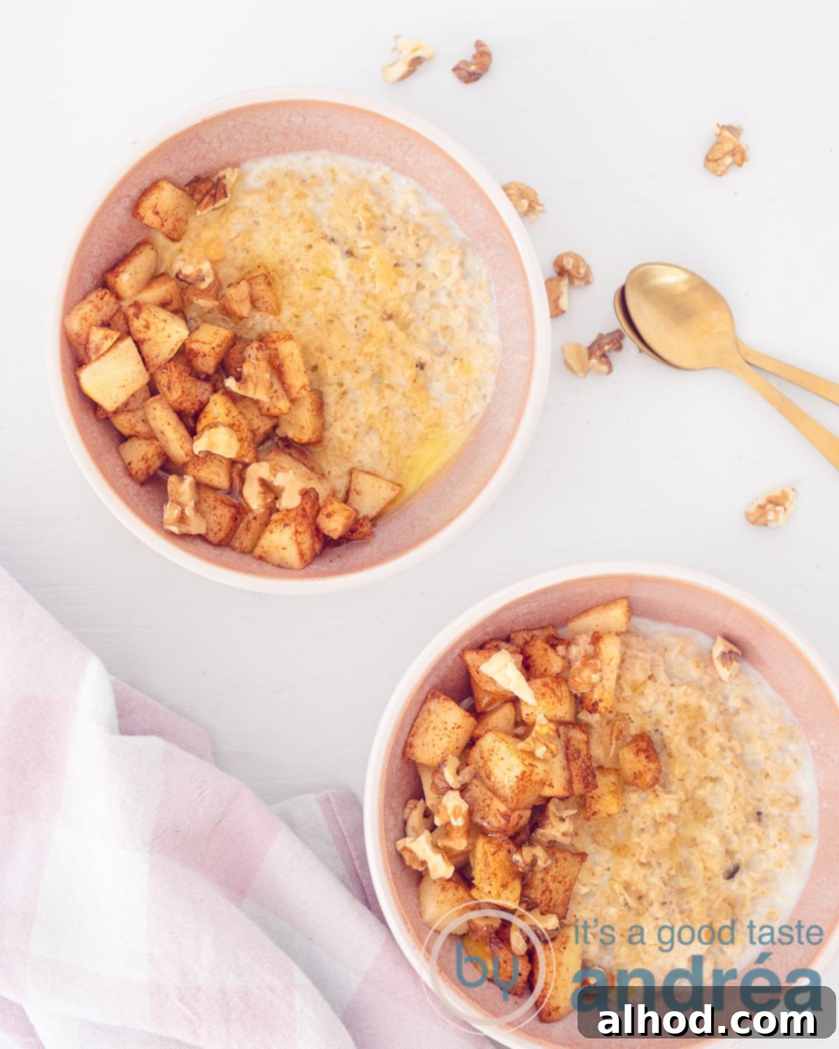 Warm Apple Cinnamon Oats 3 A photo from above of two pink bowls filled with oatmeal, gingerbread spices, apple and walnuts. At the top right two golden spoons and some walnut crumbs. At the bottom left a pink and white checkered tea towel.