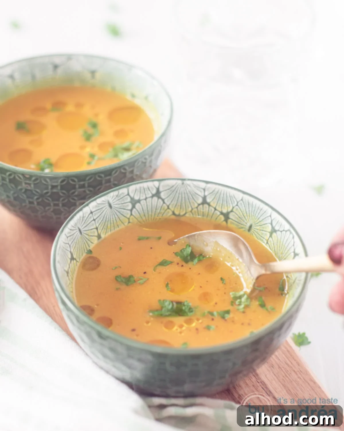 Creamy Coconut Pumpkin Soup 2 A wooden plank on a white surface. A creamy pumpkin soup with coconut milk and ginger. A spoon sticks in it.