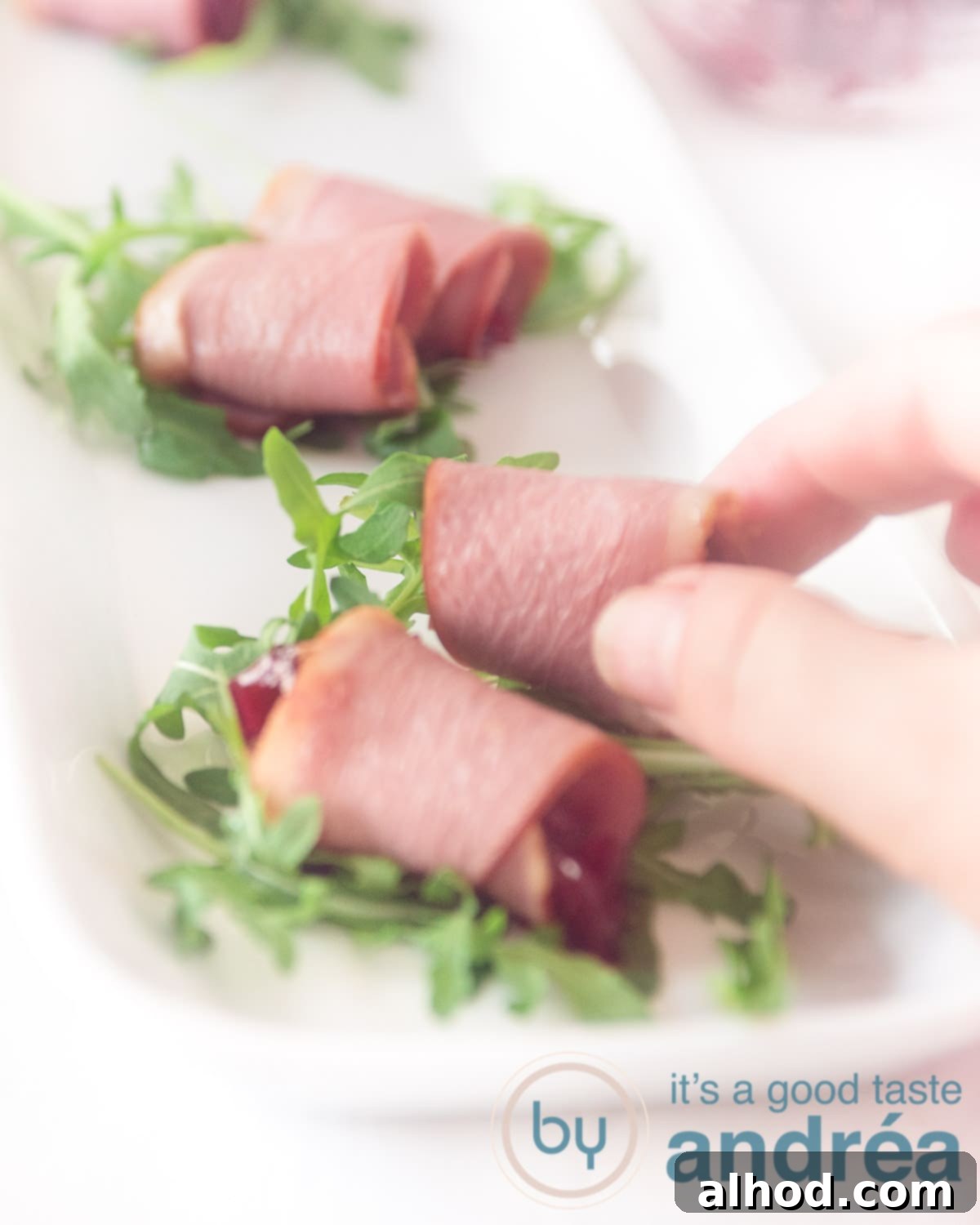Duck Breast, Cranberry, Arugula Harmony 5 A hand reaches for a perfectly rolled smoked duck breast amuse-bouche filled with cranberry compote and arugula, ready to be enjoyed.