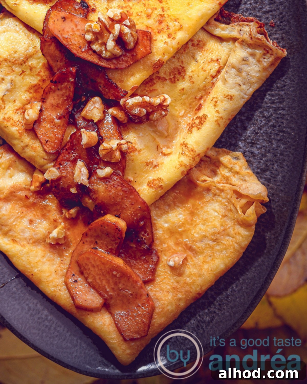 Raclette Sweet Treat: Caramelized Apple Crêpes 2 An aerial view of three delicate crêpes with caramelized apples, rich caramel sauce, and a sprinkle of walnuts on a grey platter, set against a leafy background. A small bowl of caramel sauce sits invitingly nearby.