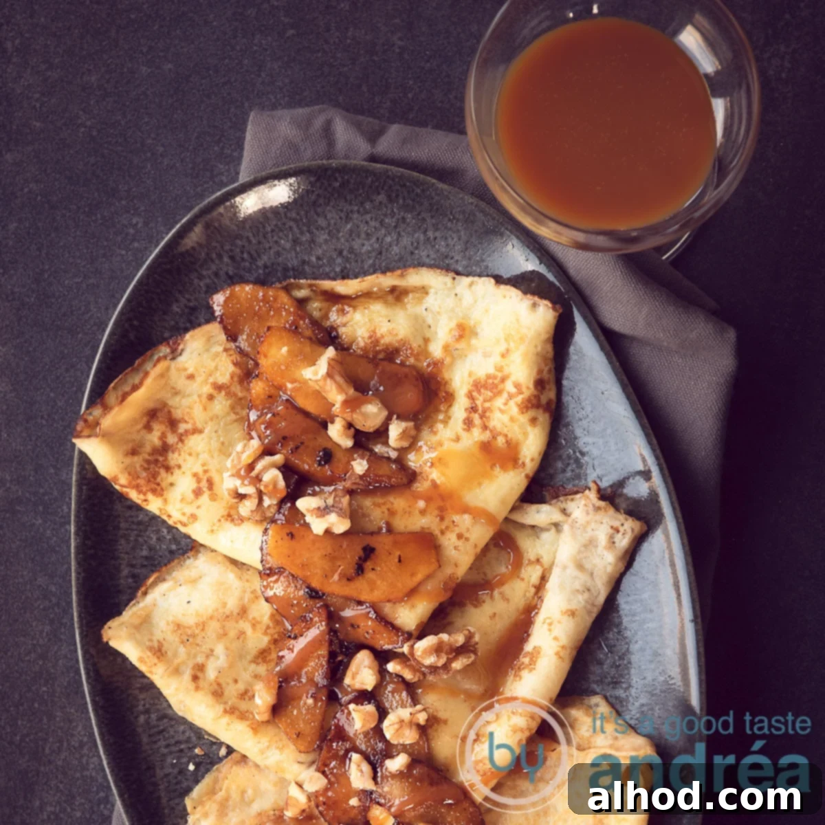 Raclette Sweet Treat: Caramelized Apple Crêpes 6 A close-up view of a grey platter featuring three delicate crêpes, each topped with caramelized apple slices and drizzled with glistening caramel sauce.