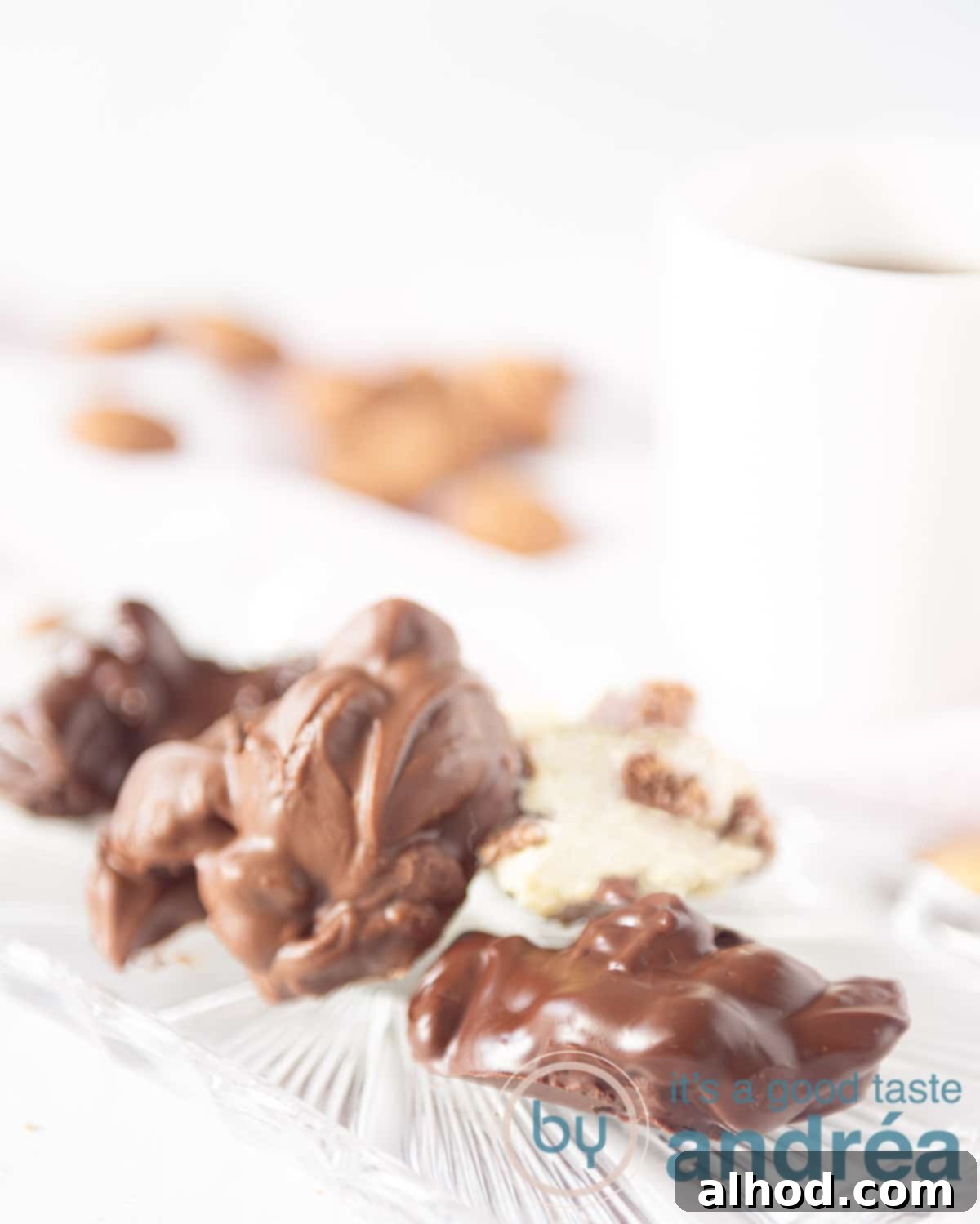 Spiced Pepernoten Chocolate Discs 2 A white backdrop. In the front a glass plate with three different kind of pepernoten chocolates. A white mug and some pepernoten in the back.