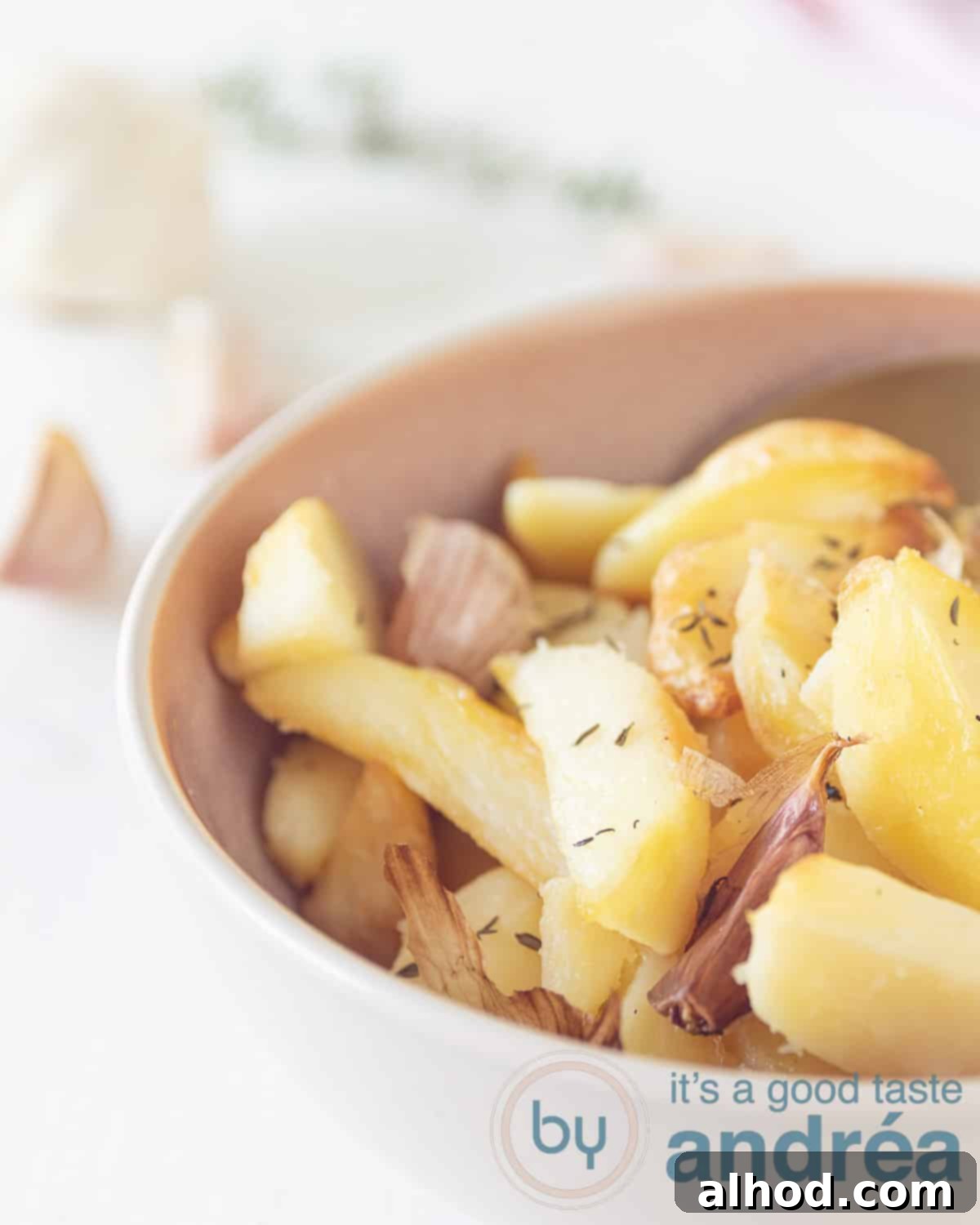 Half a bowl filled with perfectly roasted potatoes, generously seasoned with garlic and thyme. The potatoes are golden-brown and look crispy on a white background.