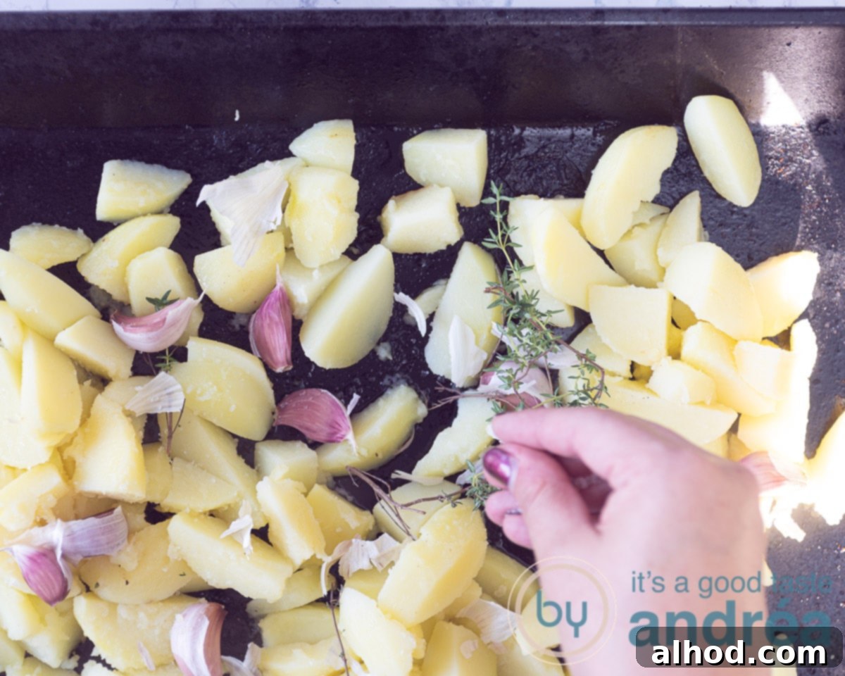 A baking plate with par-boiled potato wedges, whole garlic cloves, and fresh thyme sprigs spread evenly.