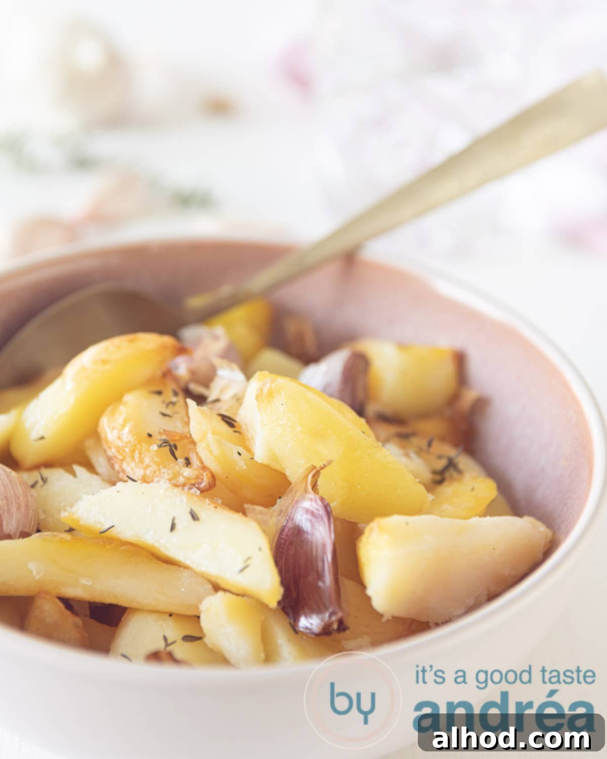 a pink bowl, roast potatoes with cloves of garlic and thyme spread on top