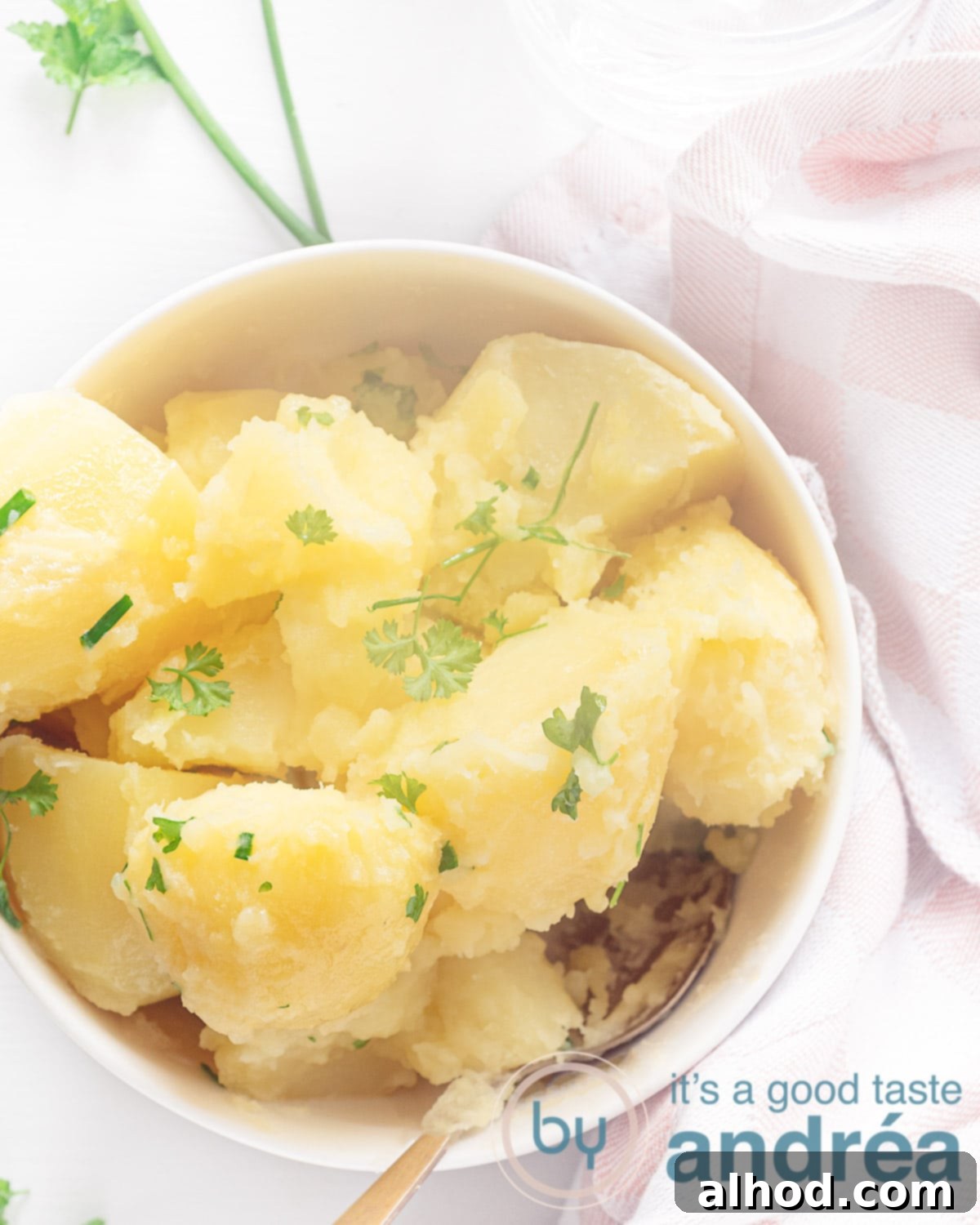 Buttery Parsley Potatoes 2 A photo from above of a white bowl filled with potatoes cooked with chives and parsley. A white background with part of a pink white tea towel