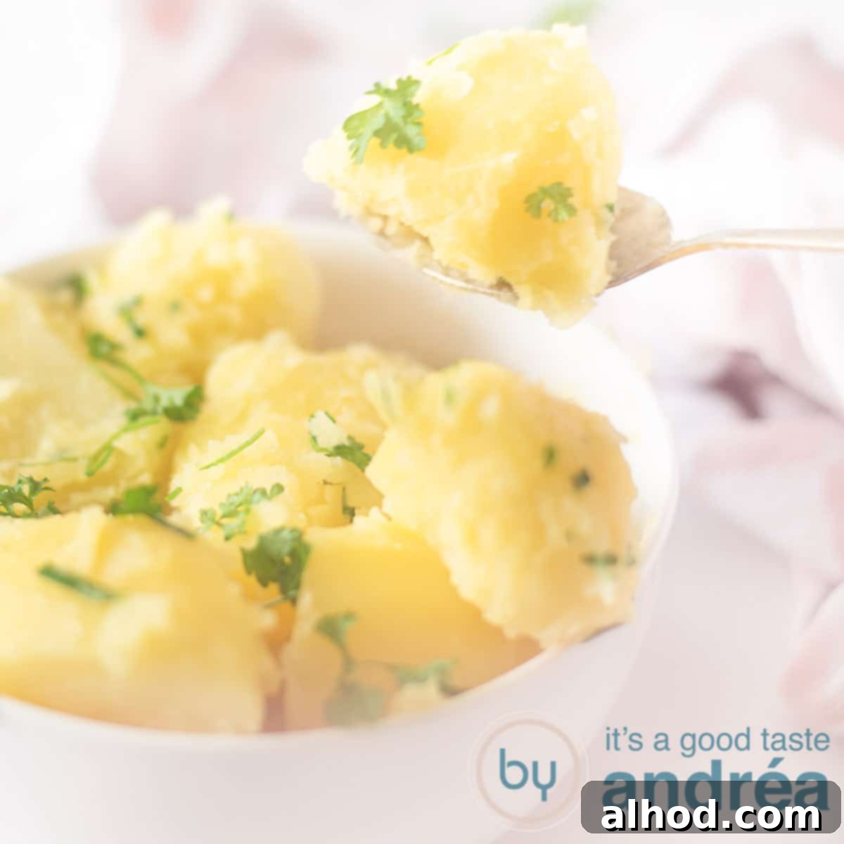 Buttery Parsley Potatoes 6 A square shot of a white bowl filled with potatoes with parsley and chives. A spoon takes out a potato on a white background