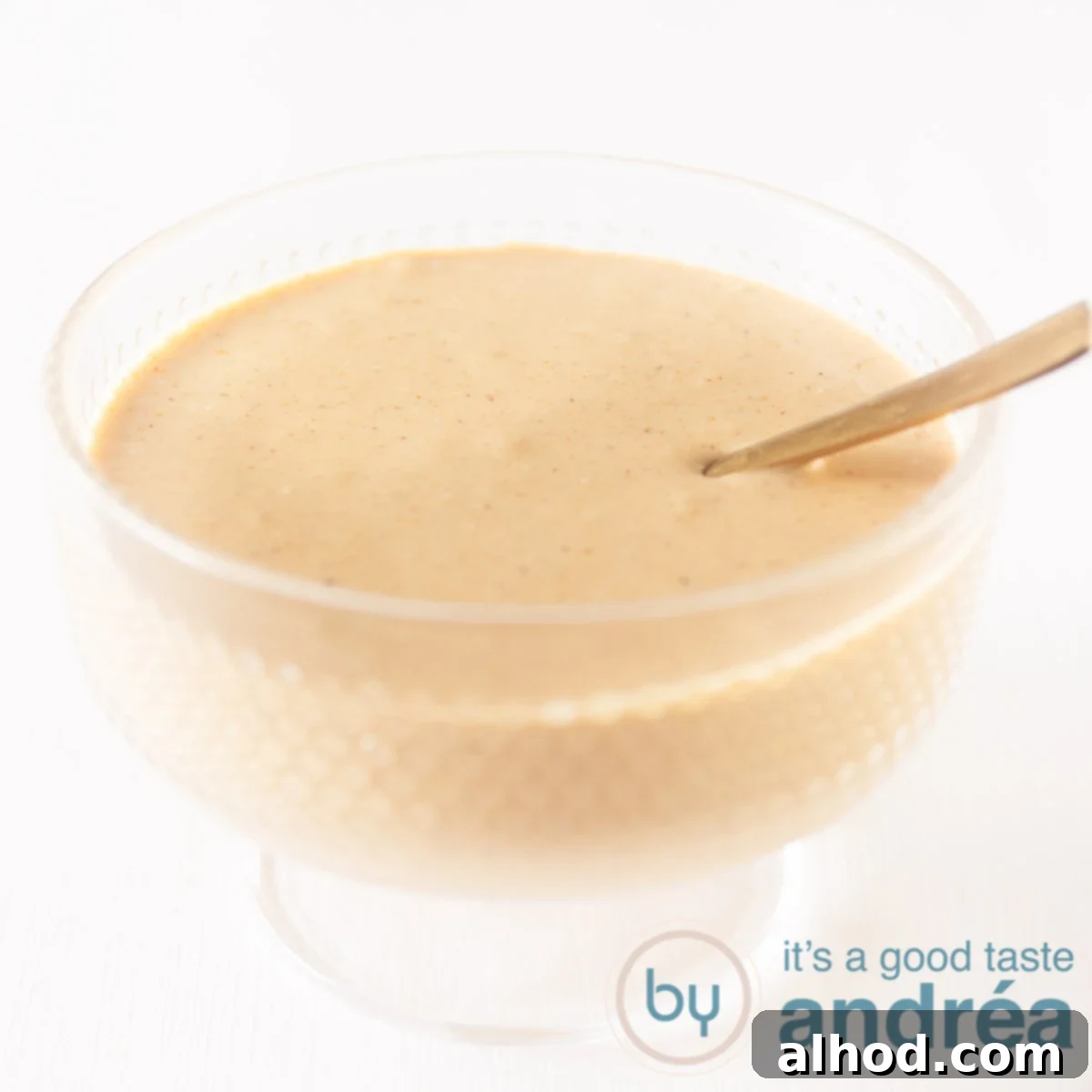 A glass bowl with creamy whiskey cocktail sauce and a golden spoon