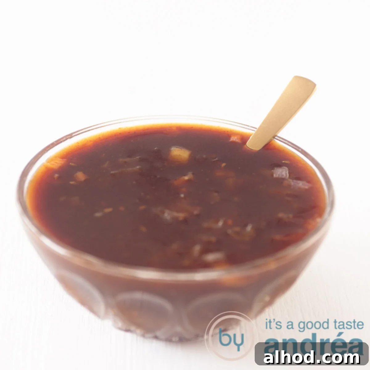 A glass bowl filled with homemade barbecue sauce with a golden spoon