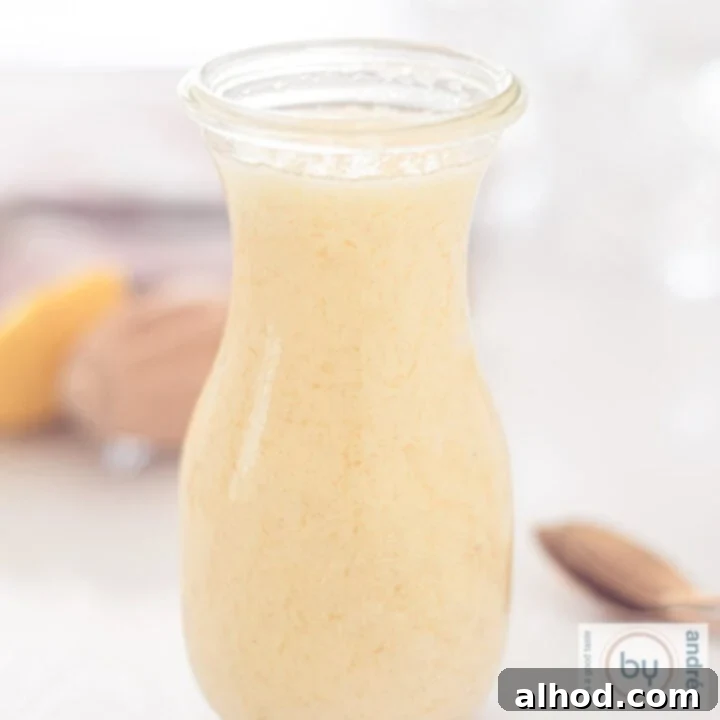 A square photo of a bottle with homemade mayonnaise and ingredients in the background