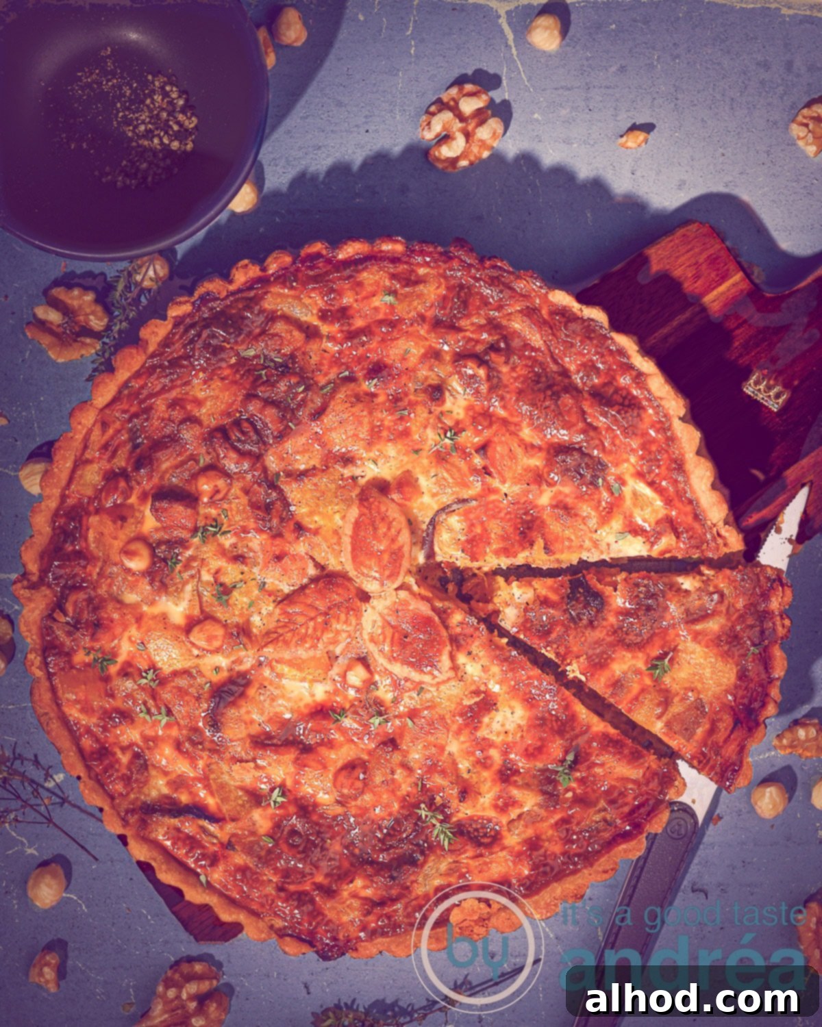 Roasted Garlic Pumpkin Sweet Potato Quiche 5 Een quiche met bladerdeeg erbovenop (blad vorm) waar een punt is uitgesneden op een blauwe ondergrond.