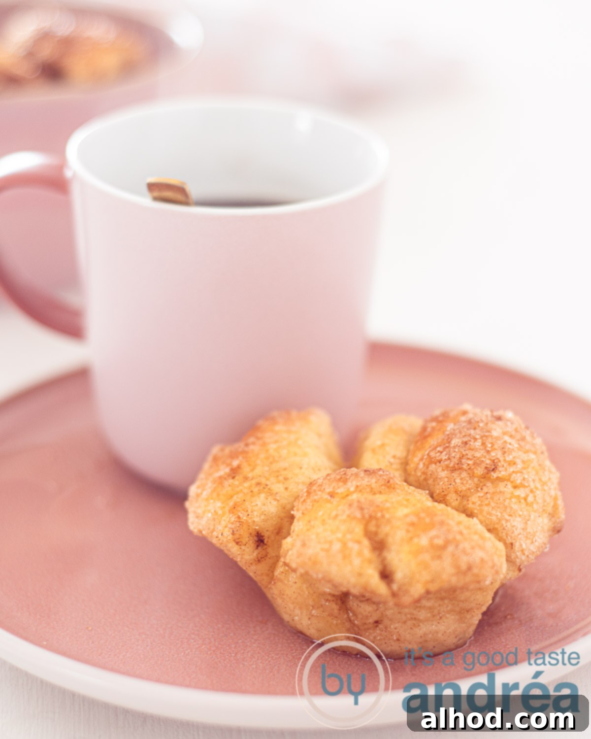 Pull-Apart Monkey Bread Muffins Recipe 5 monkey bread muffin on a pink plate with a cup of coffee at the back. A white background.