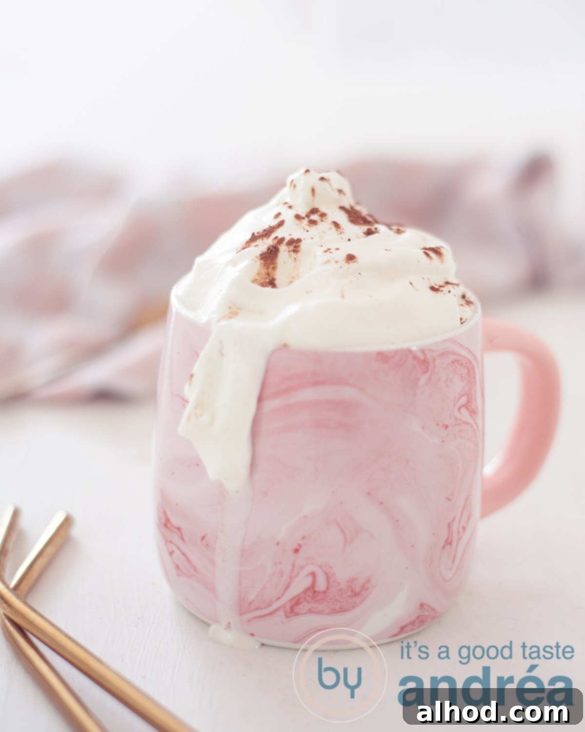 Decadent Baileys Hot Chocolate 5 hot chocolate with Baileys in a pink mug. Left For two gold straws. A white background, in the back a pink and white tea towel.
