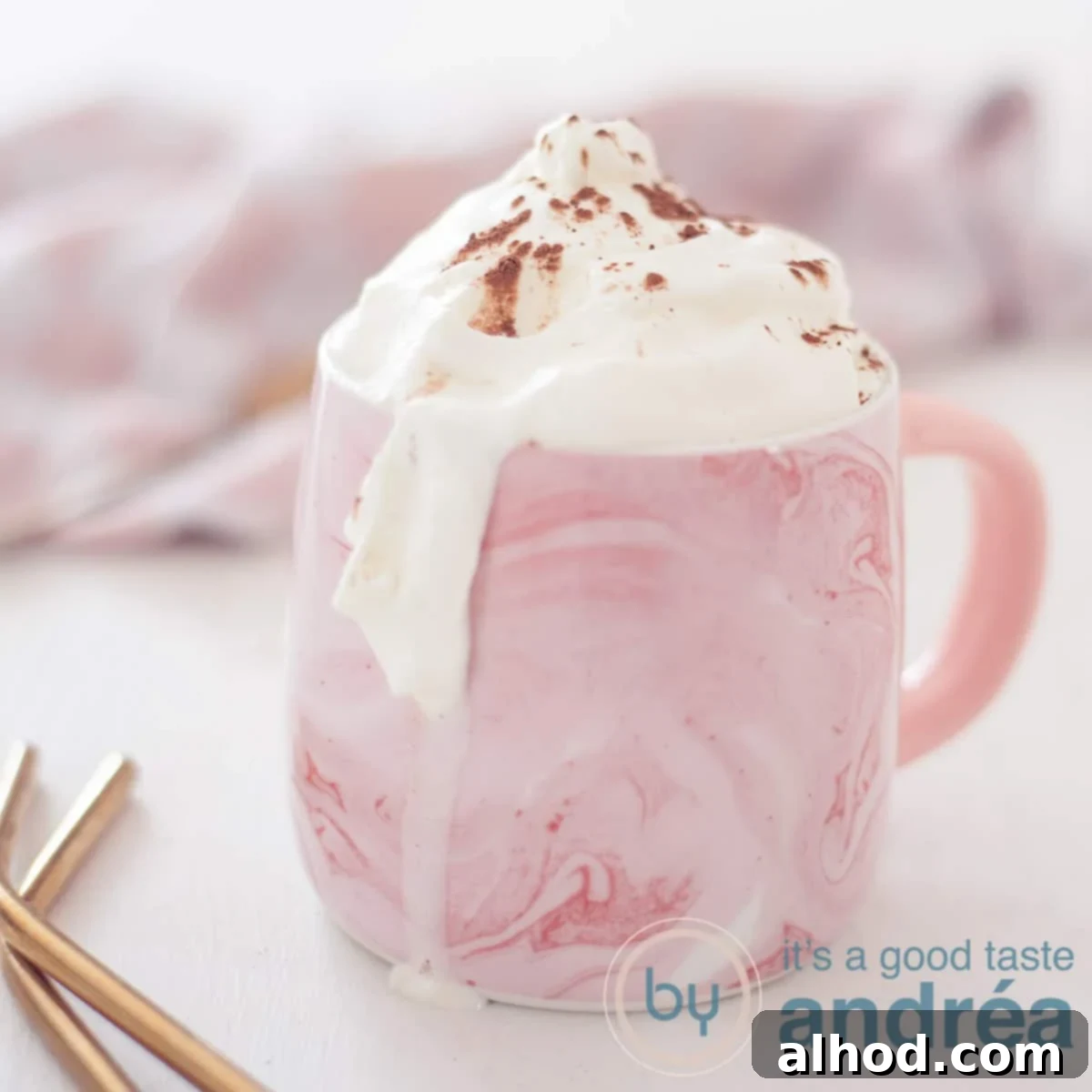 Decadent Baileys Hot Chocolate 6 A square photo of a pink mug of Baileys with hot chocolate and a whipped cream topping. A white background, in the background a pink and white tea towel. In the front left two gold straws