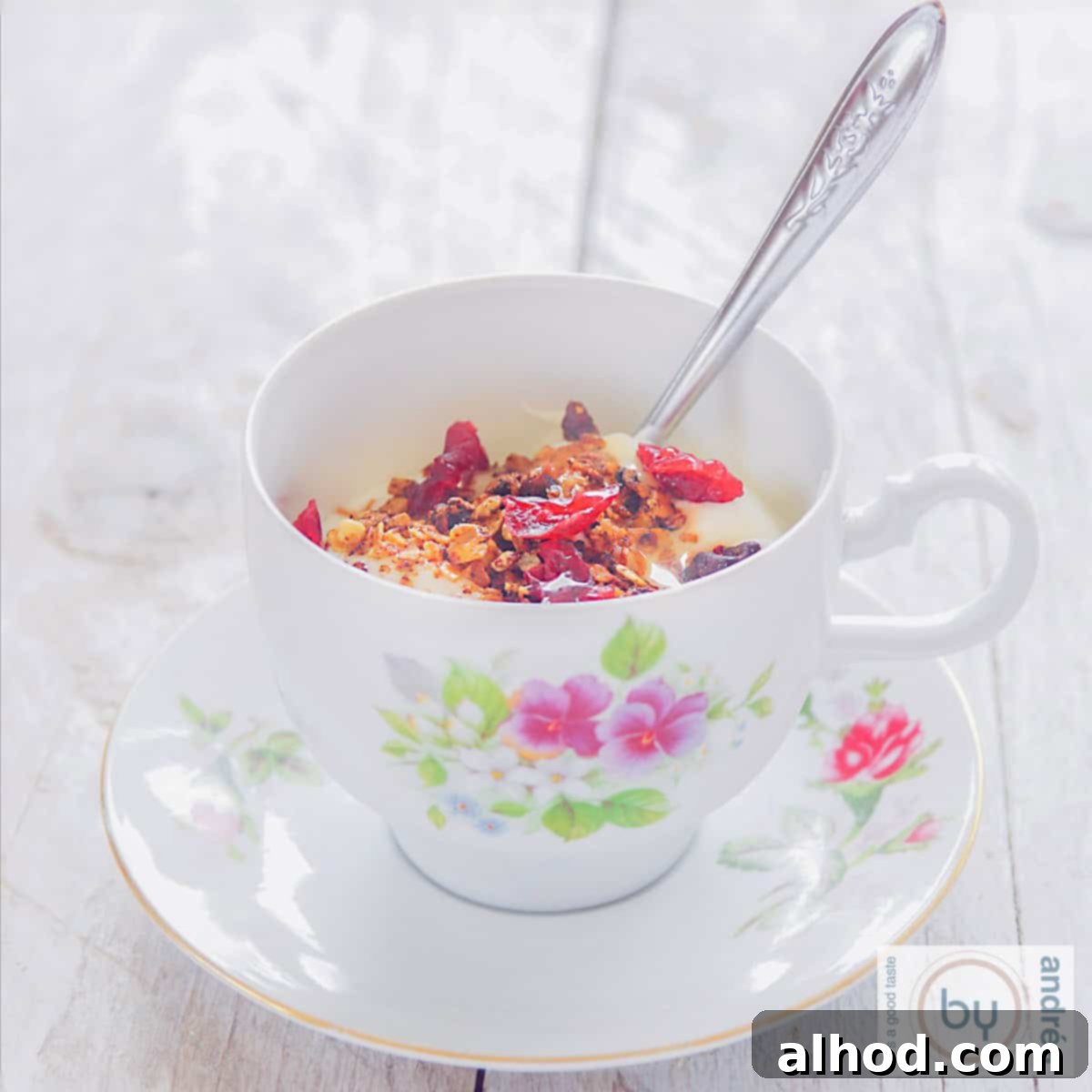 Yuletide Cranberry Pecan Crunch 4 A square image of a cup and plate filled with crunchy homemade Christmas granola, fresh yogurt, pecans, and cranberries. The inviting breakfast scene is set against a white background.
