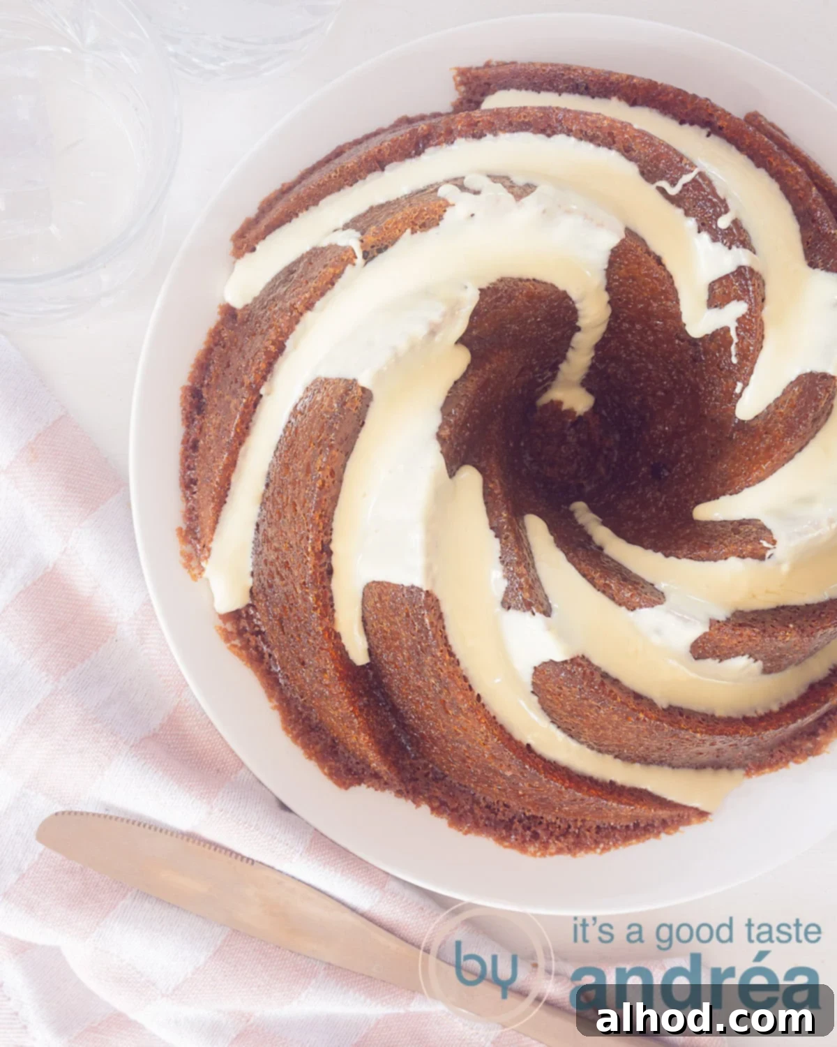 A beautiful cranberry and white chocolate bundt cake on a white plate, viewed from above, with a delicate pink and white cloth in the foreground.