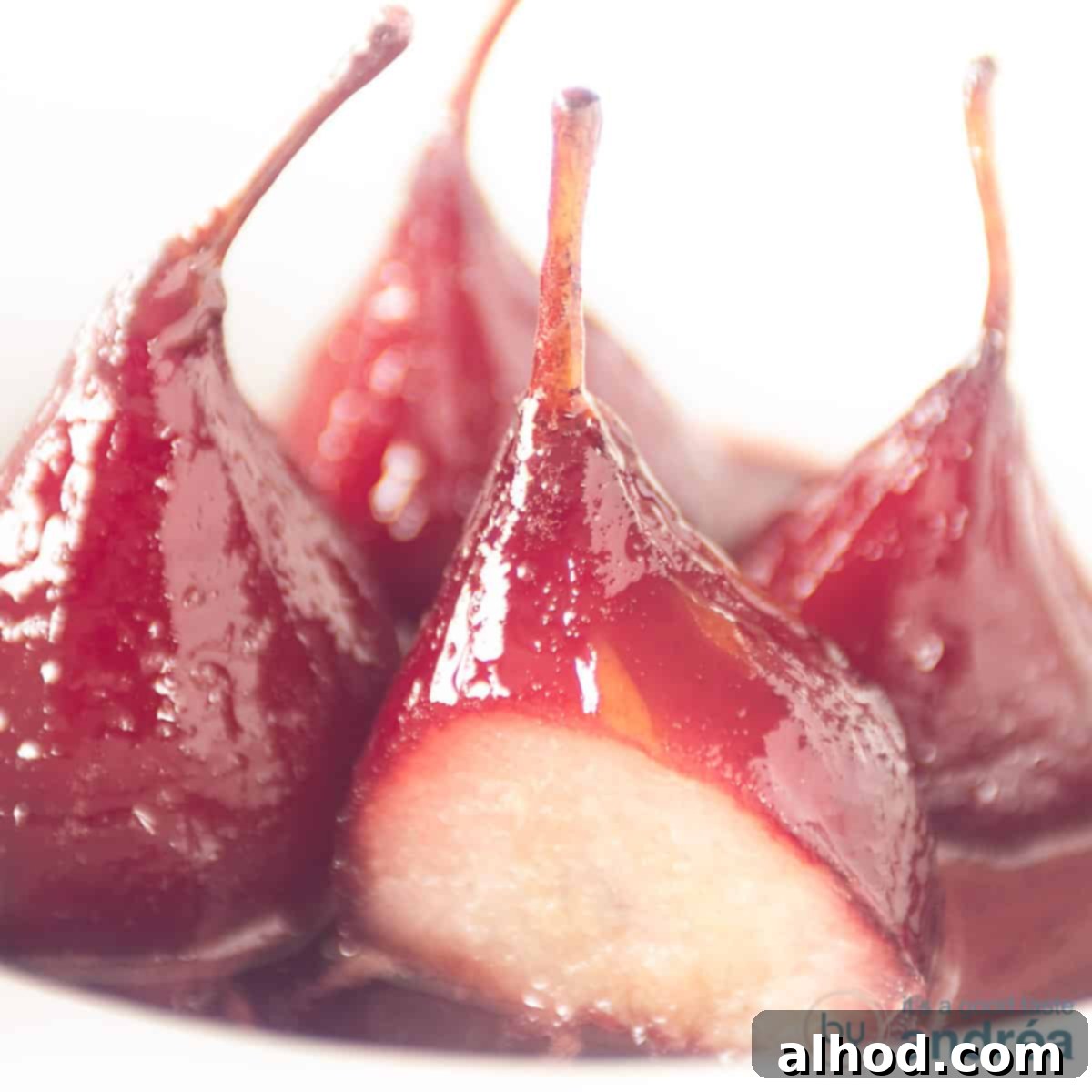 Classic French Port Wine Poached Pears Easy Recipe 6 Four poached pears on a white plate. One pear is a slice cut off.