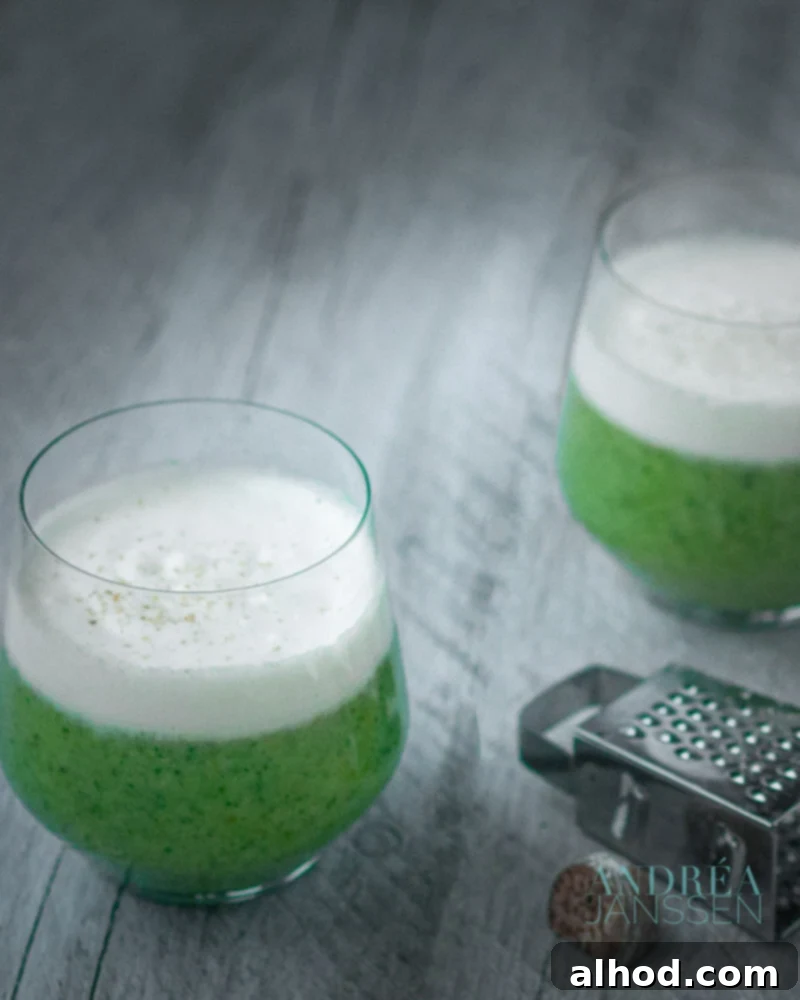 two glasses broccoli soup with a cream topping and some nutmeg