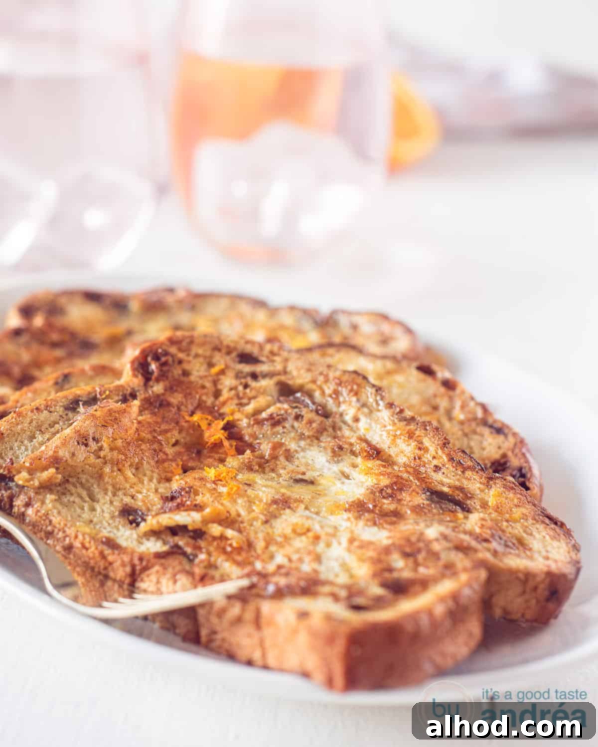 Decadent French Toast 2 French toast deluxe served on a white plate, garnished with orange zest and a drizzle of honey.