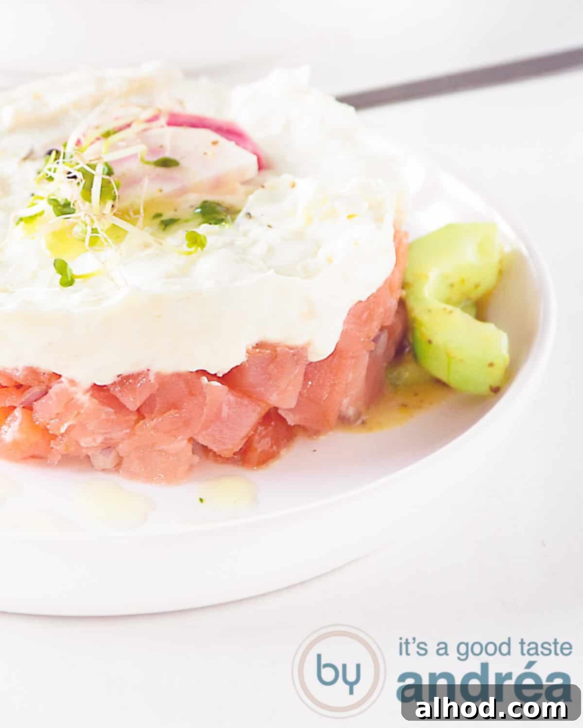 Part of a tower with salmon tartare and goat cheese mousse with honey mustard cucumber on a white plate on a white background