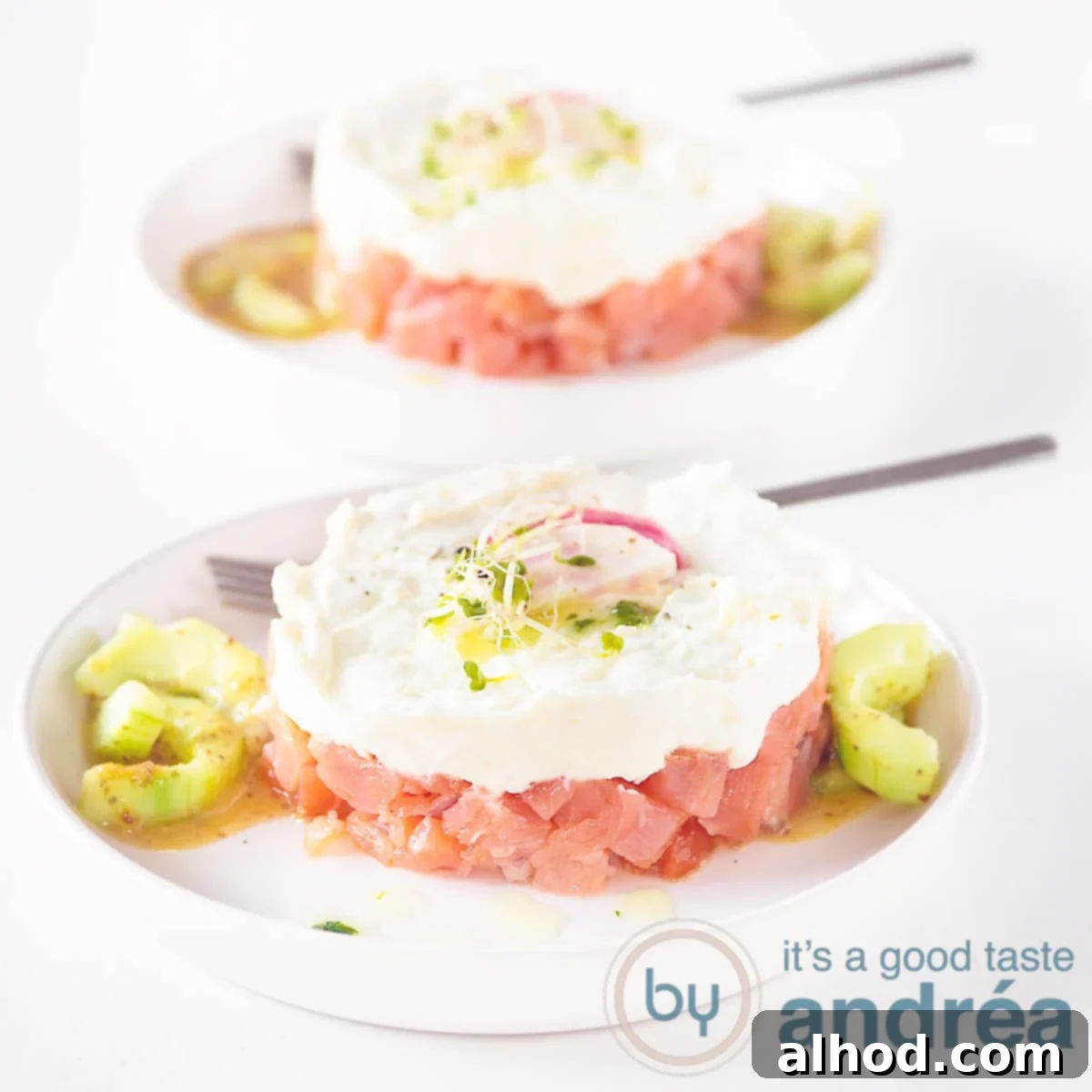 A square photo with two plates with a smoked salmon, honey and goat cheese tower on a white background.