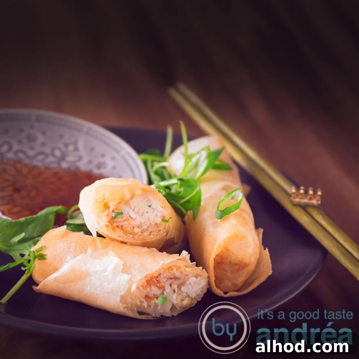 Chicken Lumpia 8 A square photo with two spring rolls on a black plate. A third chicken spring roll dipped in a sauce. In the background a wicker roll mat.