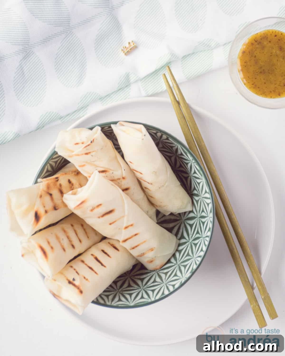 Golden Cauliflower Cheese Spring Rolls 2 A bowl filled with crispy, golden-brown grilled lumpia with cheese and cauliflower, served with a small bowl of honey dill mustard sauce in the corner.