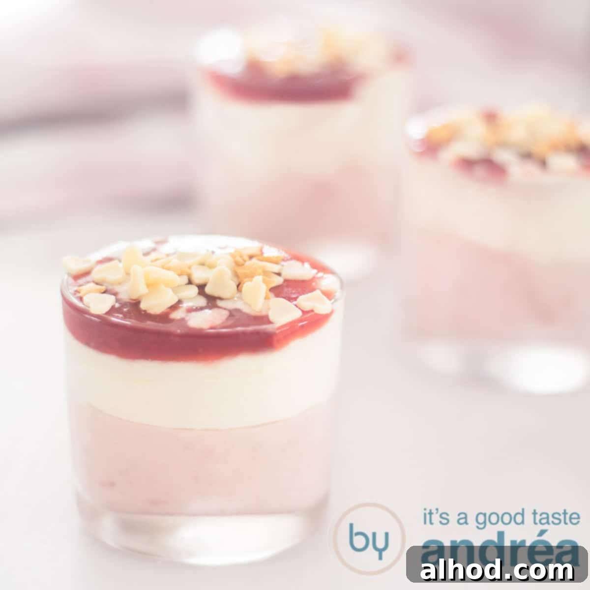 Decadent White Chocolate Strawberry Mousse 6 A square photo with three dessert glasses filled with strawberries with white chocolate mousse and a glaze. A pink white towel in the background