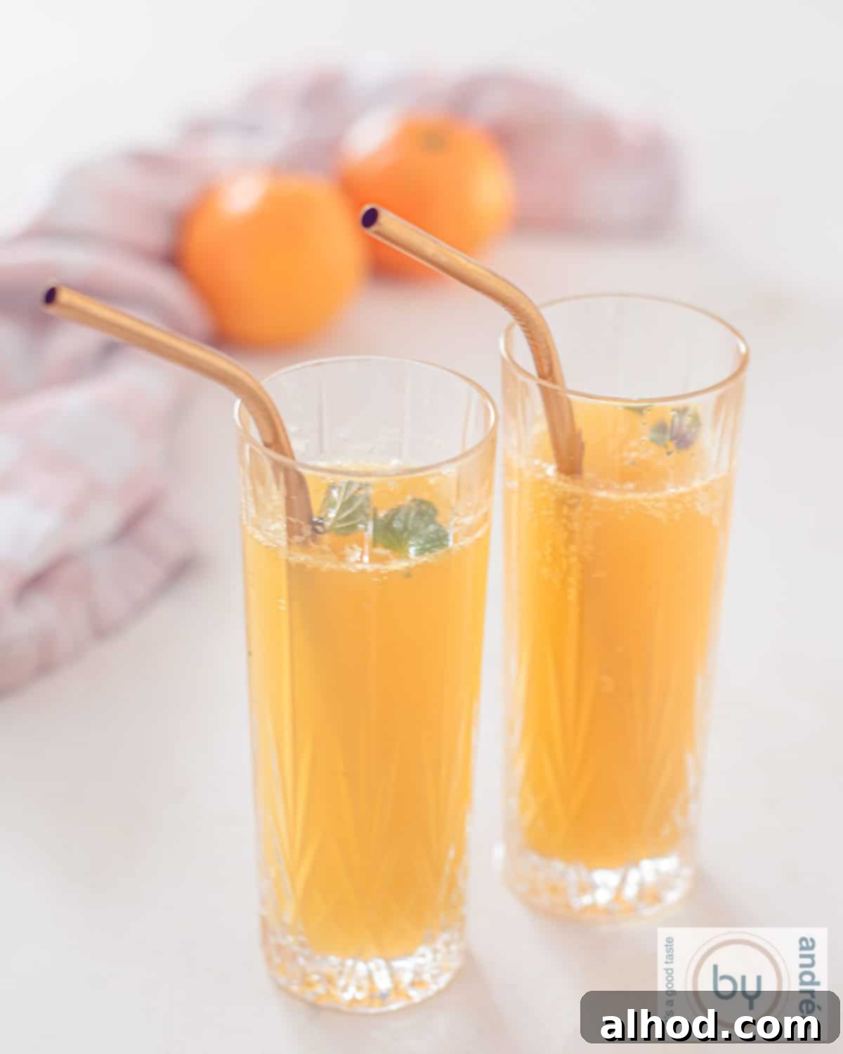 A height shot of two glasses filled with Tangerine Mimosa with Cointreau with golden straws.