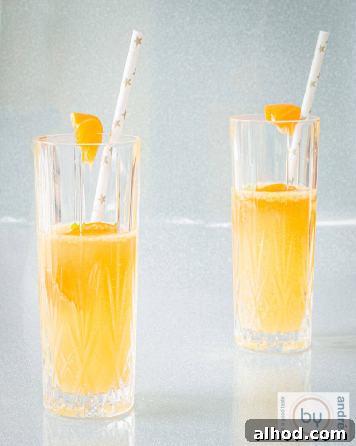 A height photo of two glasses filled with a cocktail of mandarin, champagne and cointreau on a silver background.
