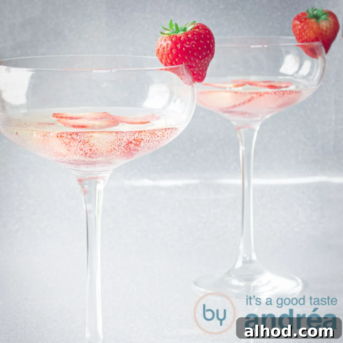 A square photo of two champagne glasses filled with Prosecco and fresh strawberries on a silver background, highlighting a refreshing and vibrant cocktail.