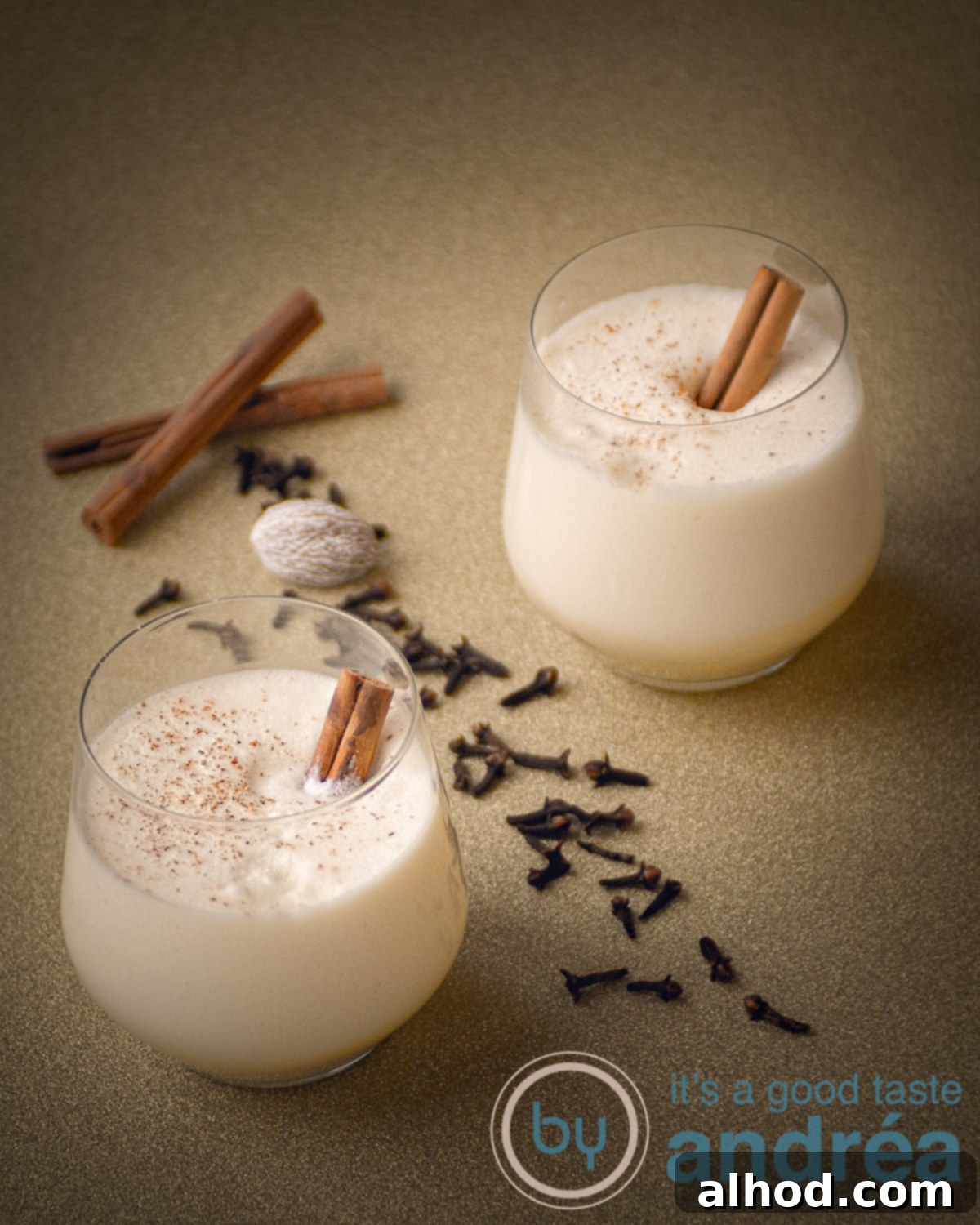 Traditional egg nog in two glasses on a golden underground. Some spices are scattered around, creating a warm and inviting holiday scene.