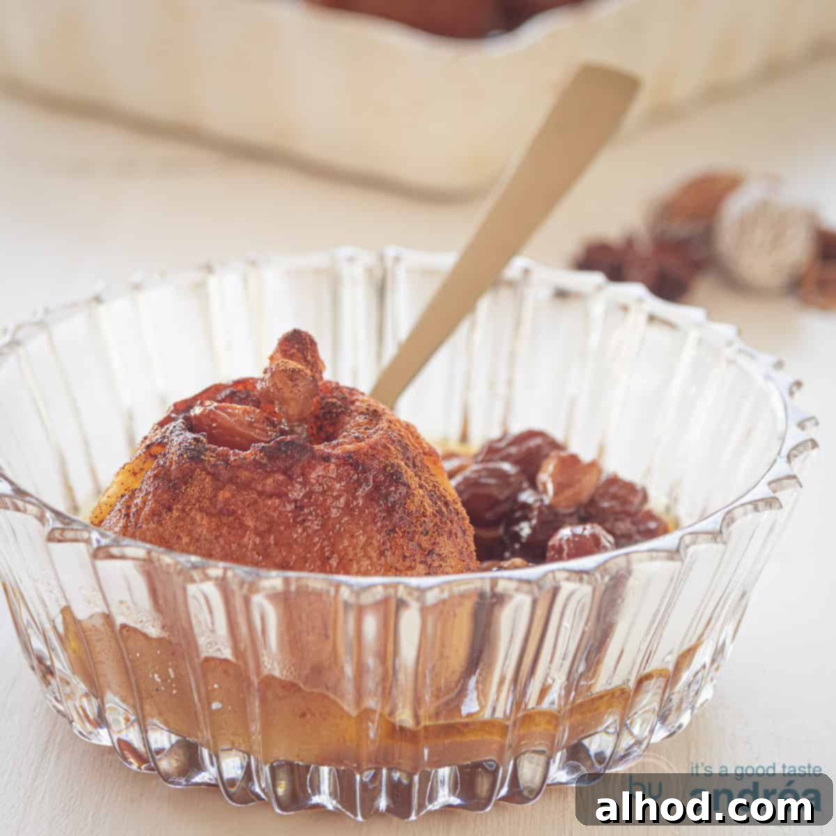 A square photo with a glass bowl with a stuffed apple and a raisin caramel sauce around it. A white background.