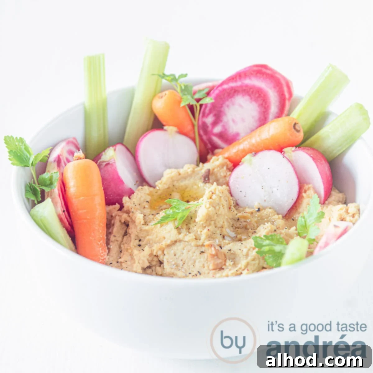 Zesty Lemon Garlic Hummus 6 A square photo with a white bowl filled with hummus with carrots, radishes and celery in it.