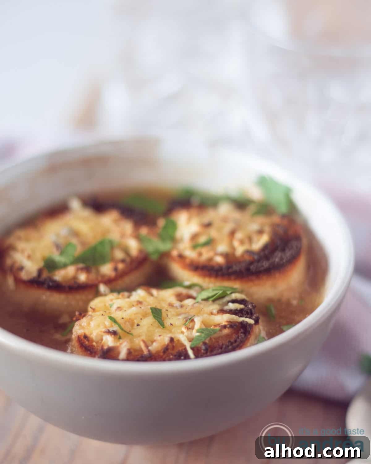 Simple Beer French Onion Soup 2 A height photo of a gray bowl of beer onion soup with three baguettes floating on top with gratinated cheese. On a wooden plank.