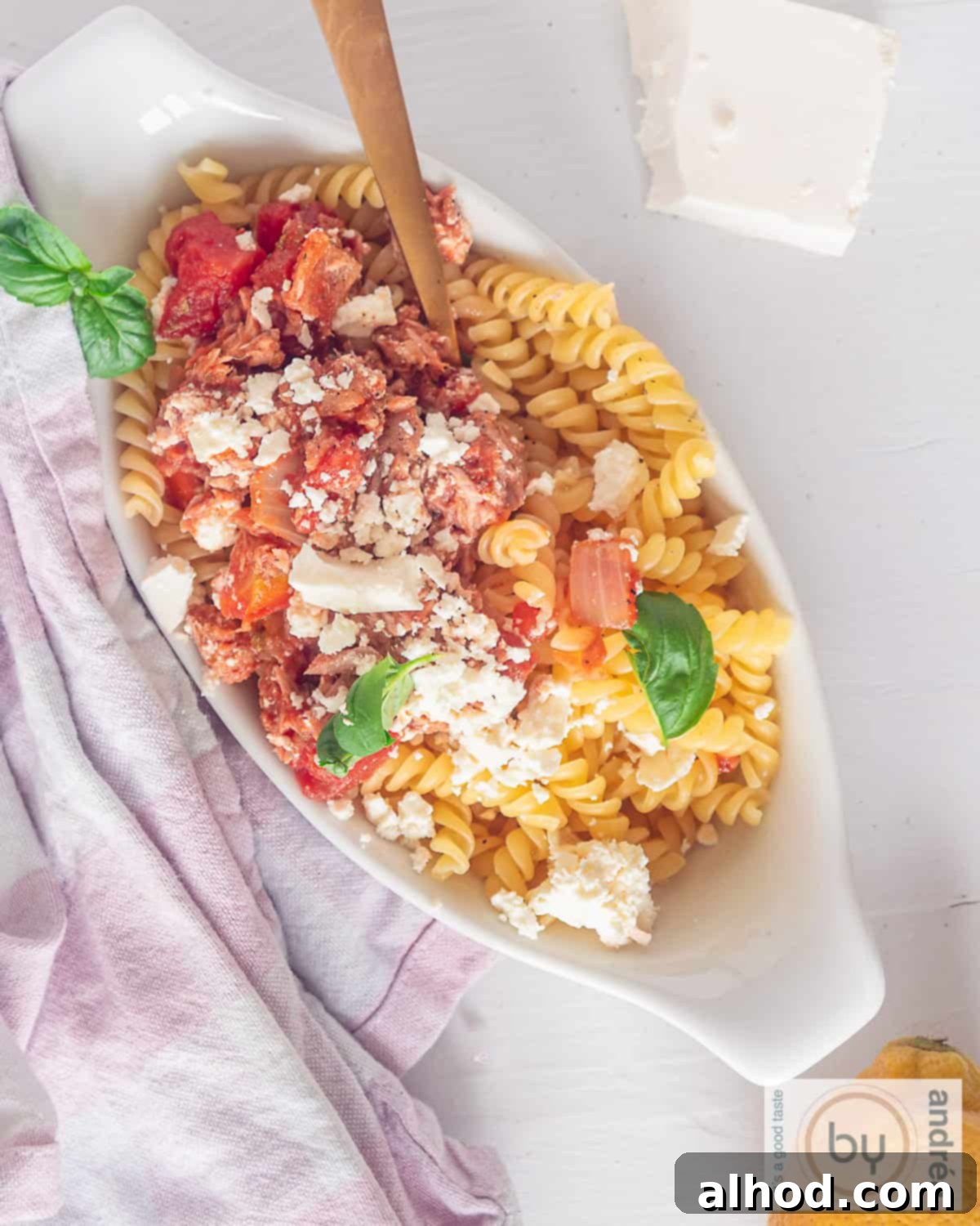20-Minute Mediterranean Tuna Feta Pasta 3 A top-down photo of a white bowl of pasta, tuna, feta, and tomato sauce, garnished with fresh herbs.