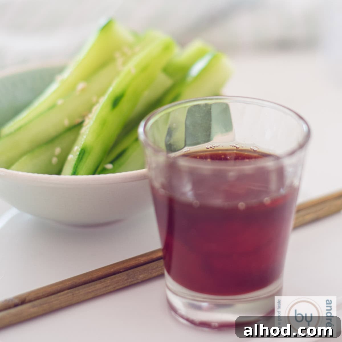 Healthy Bites for Afternoon Energy 3 A square photo featuring a bowl of crisp cucumber strips topped with sesame seeds. In the foreground, two chopsticks rest beside a small glass filled with a vibrant, spicy dipping sauce, inviting a refreshing and flavorful snack experience.