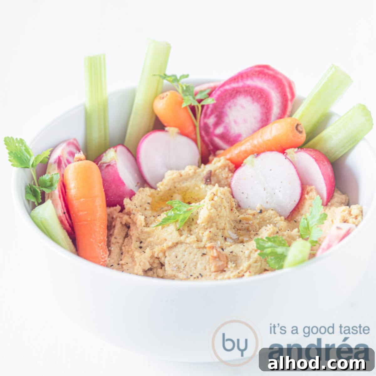 Healthy Bites for Afternoon Energy 8 A square photo featuring a pristine white bowl generously filled with creamy hummus. Vibrant carrot sticks, crisp radishes, and fresh celery stalks are artfully arranged within and around the hummus, creating an inviting and healthy dipping snack.