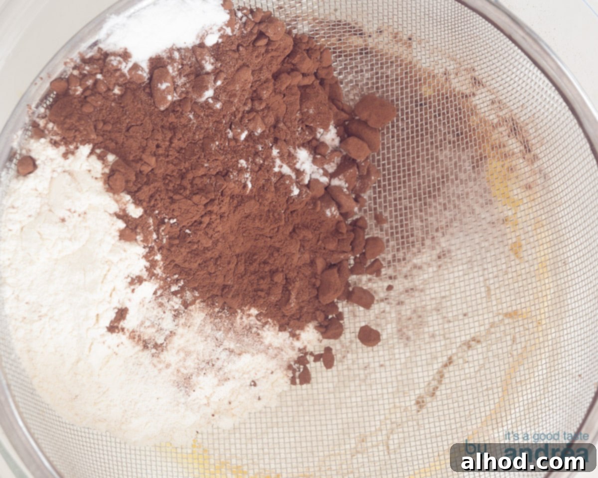 Easy Dairy-Free Chocolate Cupcakes 6 A fine-mesh sieve is placed over a bowl of wet ingredients, and dry ingredients, including flour, cocoa powder, baking soda, and salt, are being carefully sifted into the liquid mixture for the cupcake batter.
