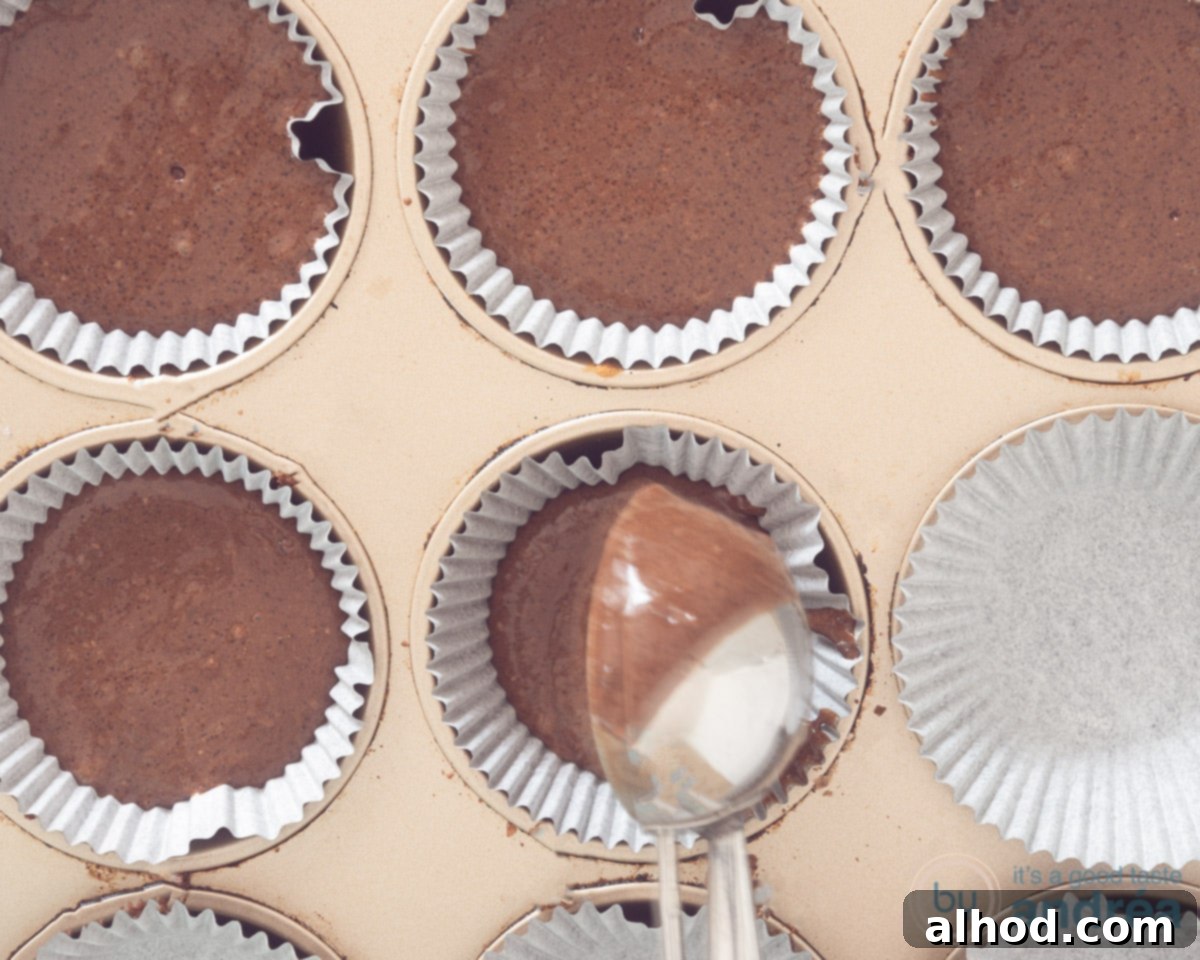 Easy Dairy-Free Chocolate Cupcakes 7 Cupcake batter being precisely scooped into individual paper liners within a muffin tin using an ice cream scoop, ensuring each cupcake is evenly portioned before baking.