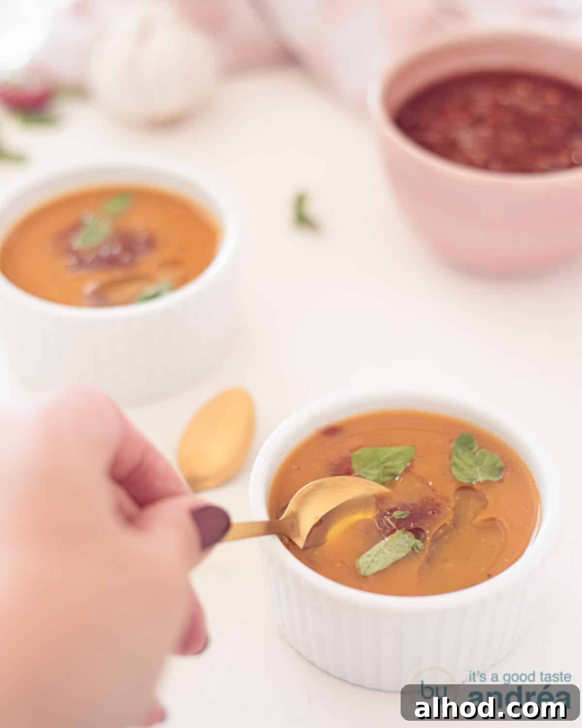 Wholesome Kickin' Pumpkin Warmth 2 Two bowls filled with spicy pumpkin soup with salsa diagonally behind each other. A spoon takes a bite. A bowl of salsa in the background