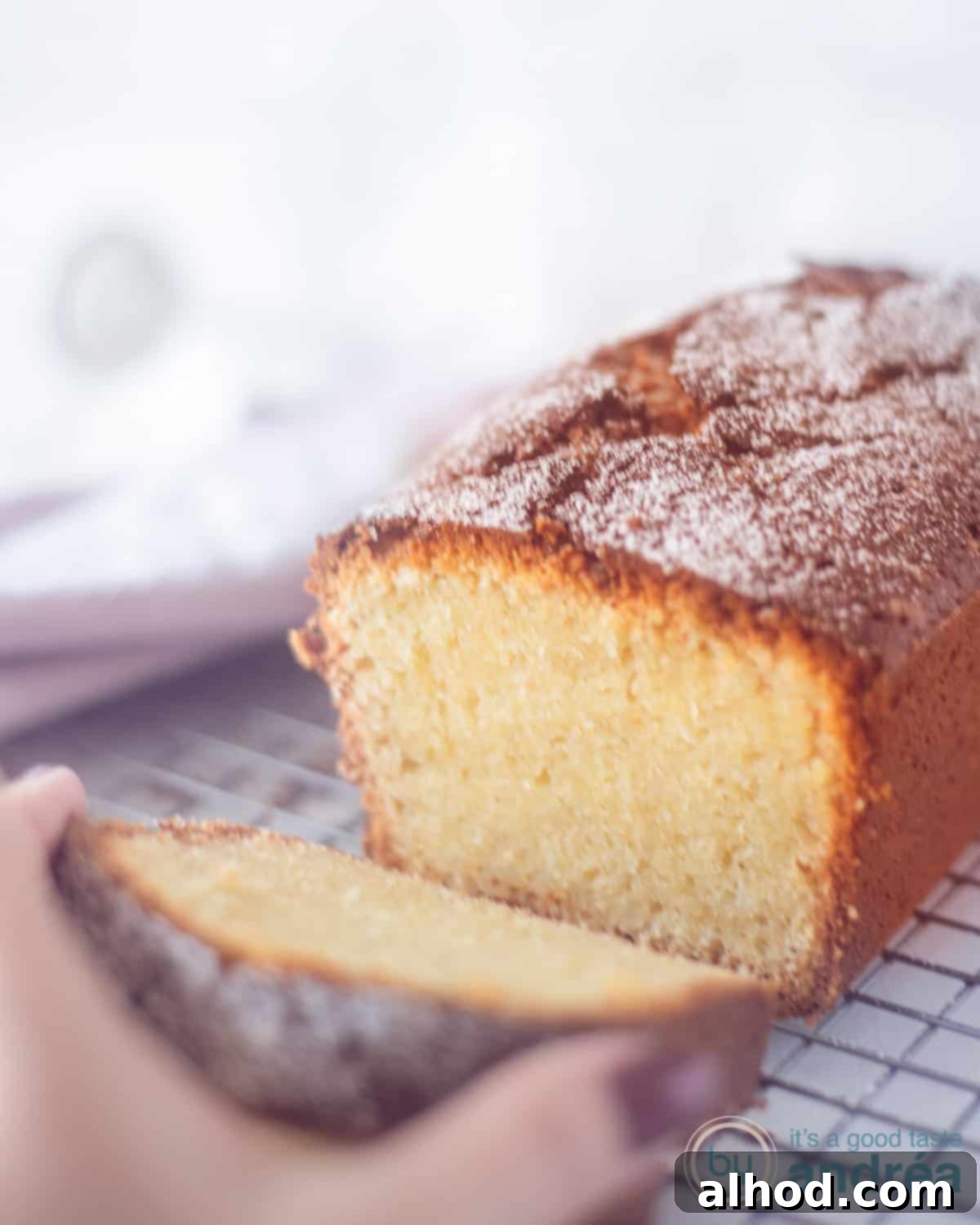 Effortless Cream Cheese Pound Cake Perfection 2 A cream cheese cake on a rack with a slice cut off. A hand grabs the slice, showcasing its moist texture and golden crust.