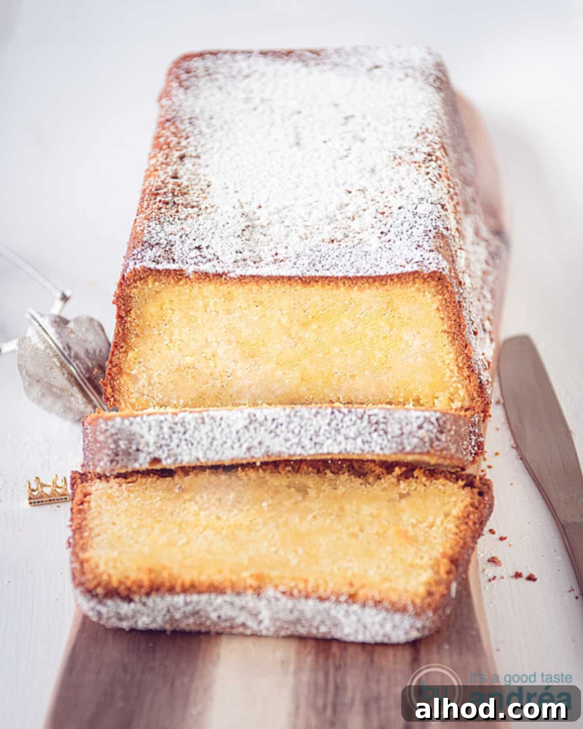 Effortless Cream Cheese Pound Cake Perfection 3 Cream cheese pound cake on a wooden board on a white surface, generously sprinkled with powdered sugar. Two slices are neatly cut off and presented in front.