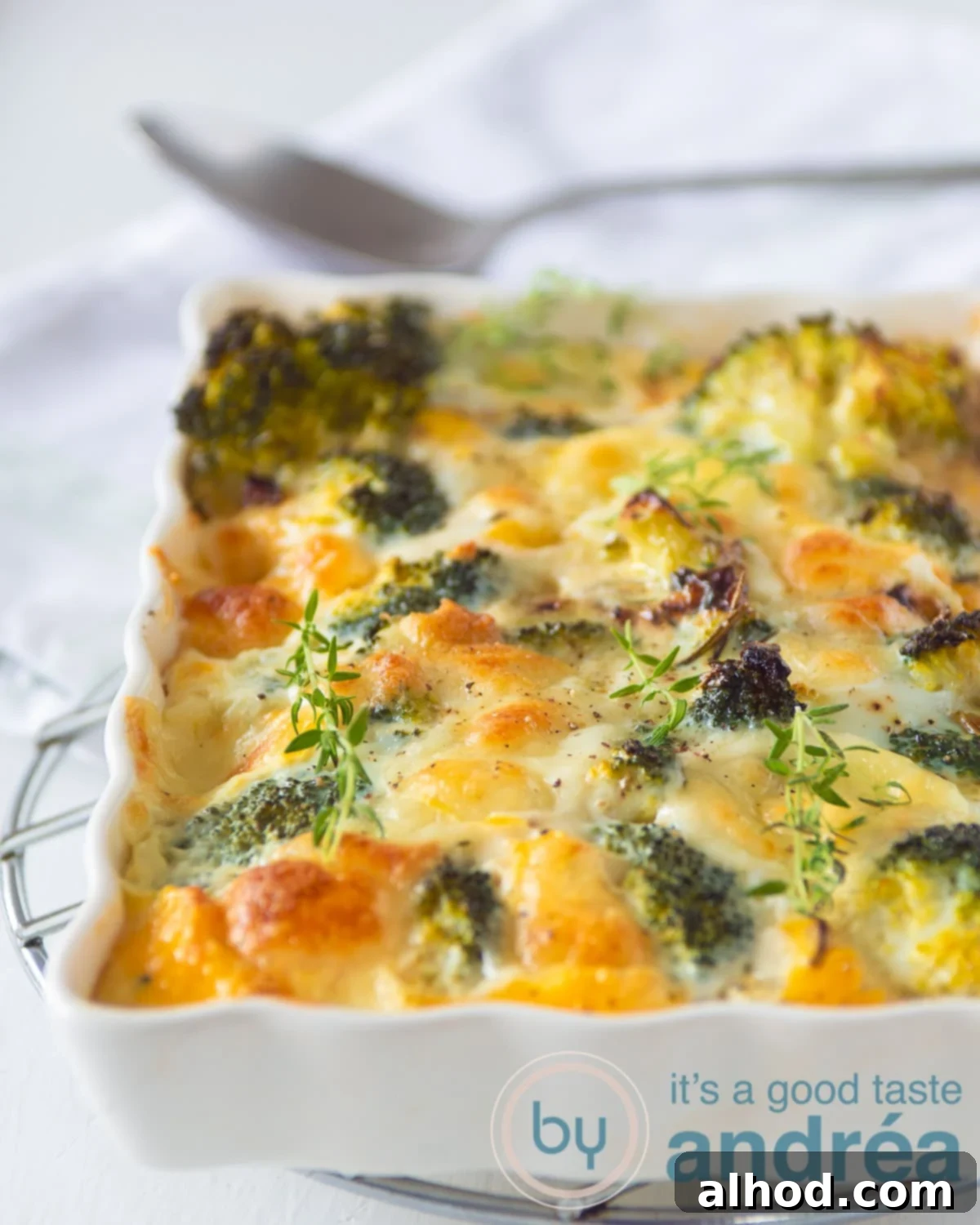 Herby Broccoli Frittata with Melted Mozzarella 7 Golden-brown Broccoli Mozzarella Frittata in a white ceramic casserole dish on a clean white background, with a serving spoon nearby.