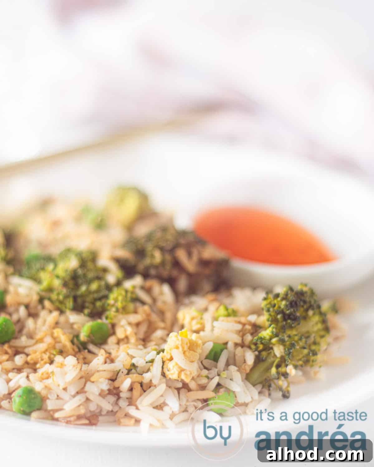Quick Broccoli Egg Fried Rice 2 An elevation photo showing a white plate with fried rice, egg, broccoli and peas. Top a bowl with sweet chili sauce. A white background.