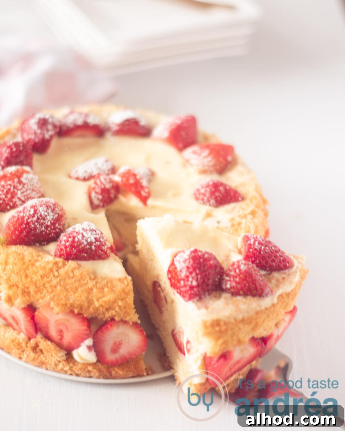 Cloud-Soft Strawberry Chiffon 2 A photo diagonally above of a strawberry sponge cake on a white background. A cake server takes a point out