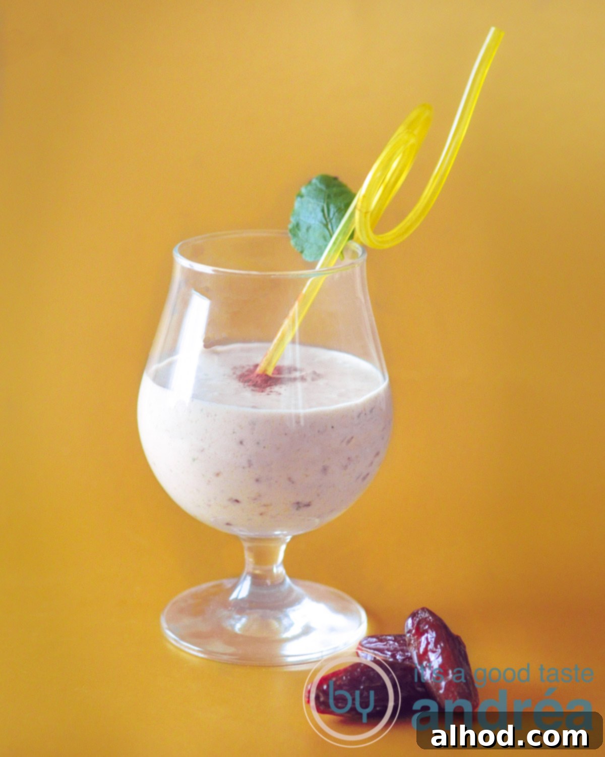 Tropical Mango Date Coconut Dream 2 A golden yellow background with a glass filled with tropical vegan smoothie, a yellow straw and a dash of cinnamon. Three dates layng in front.